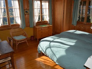 A wooden room with a bed, a chair, a dresser, and a window with curtains.
