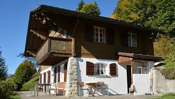 Una casa a due piani in legno con un balcone, un pilastro in pietra e un'area salotto esterna.