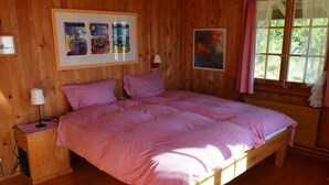 Una stanza in legno con un letto, un comodino, una lampada e una finestra con tende.
