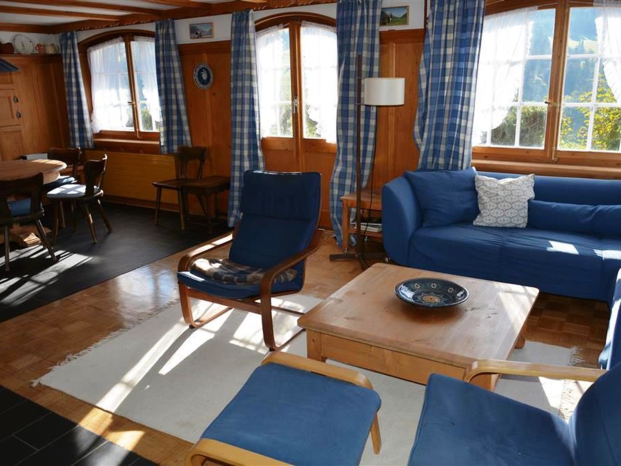 A room with a blue sofa, a wooden chair, a small table, and a dining table with chairs.