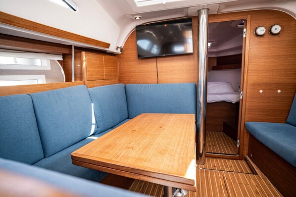 Un intérieur compact comprenant une table en bois, des sièges rembourrés bleus, un téléviseur et un petit espace de couchage fermé.