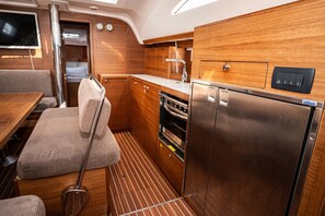 A compact kitchen with wooden cabinets, a stainless steel refrigerator, and a small dining area with a table and cushioned seating. - Sibenik Sun-soaked Sailing: A Luxurious Croatian Voyage (Pirovac)