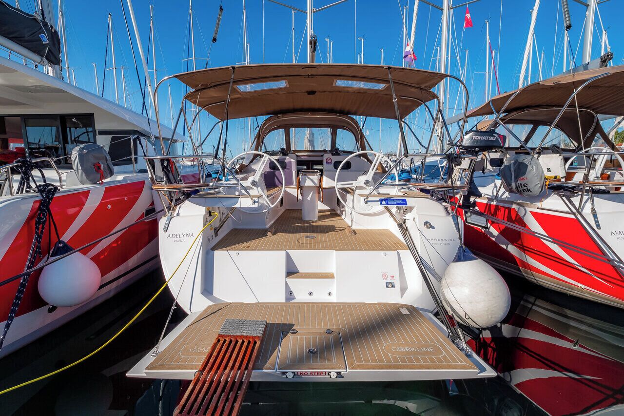 A marina with multiple sailboats docked, featuring a central boat with a covered deck and a name 'ADELYNA' visible.