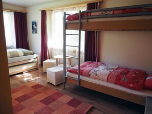 A bunk bed room with a small table and a chair, a window with curtains, and a wooden floor. - Am Ryschbächli Appartement/Fewo, Dusche oder Bad, WC 6-Bettwohnung by Interhome (Zweisimmen)