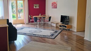 A living room with a dining area, a TV, and a large window with curtains. - Am Ryschbächli Appartement/Fewo, Dusche oder Bad, WC 6-Bettwohnung by Interhome (Zweisimmen)