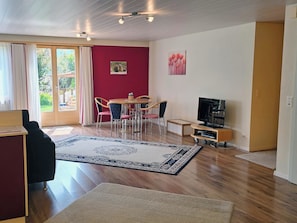 Ein Wohnzimmer mit Essbereich, einem Fernseher und einem großen Fenster mit Vorhängen.