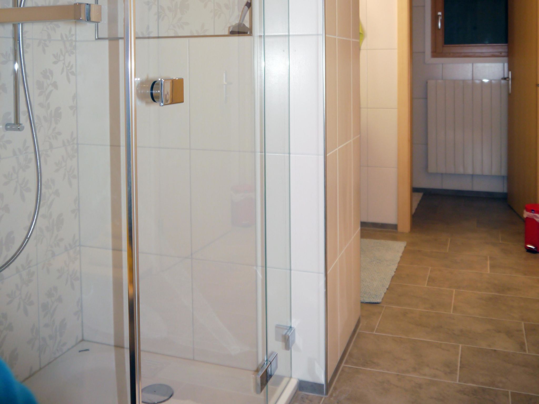 A bathroom with a glass shower enclosure, white tiled walls, and a brown tiled floor.