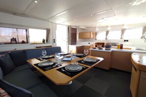 A compact kitchen with a dining area, featuring a table set for four, a sofa, and a small kitchenette. - Sun-Kissed Sailing Adventure in Islas Sarónicas (Alimos)
