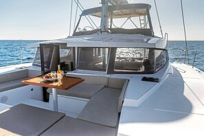 A yacht with a dining area featuring a table, cushions, and a view of the sea. - Sun-Kissed Sailing Adventure in the Sporades Islands from Volos, Thessaly (Volos)