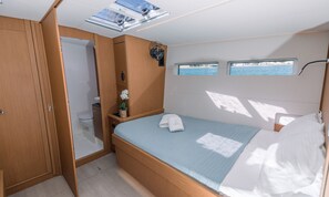 A compact bedroom with a bed, a small window, a ceiling fan, and a view of the sea. - Sun-Kissed Sailing Adventure in the Saronic Islands (Nea Peramos)