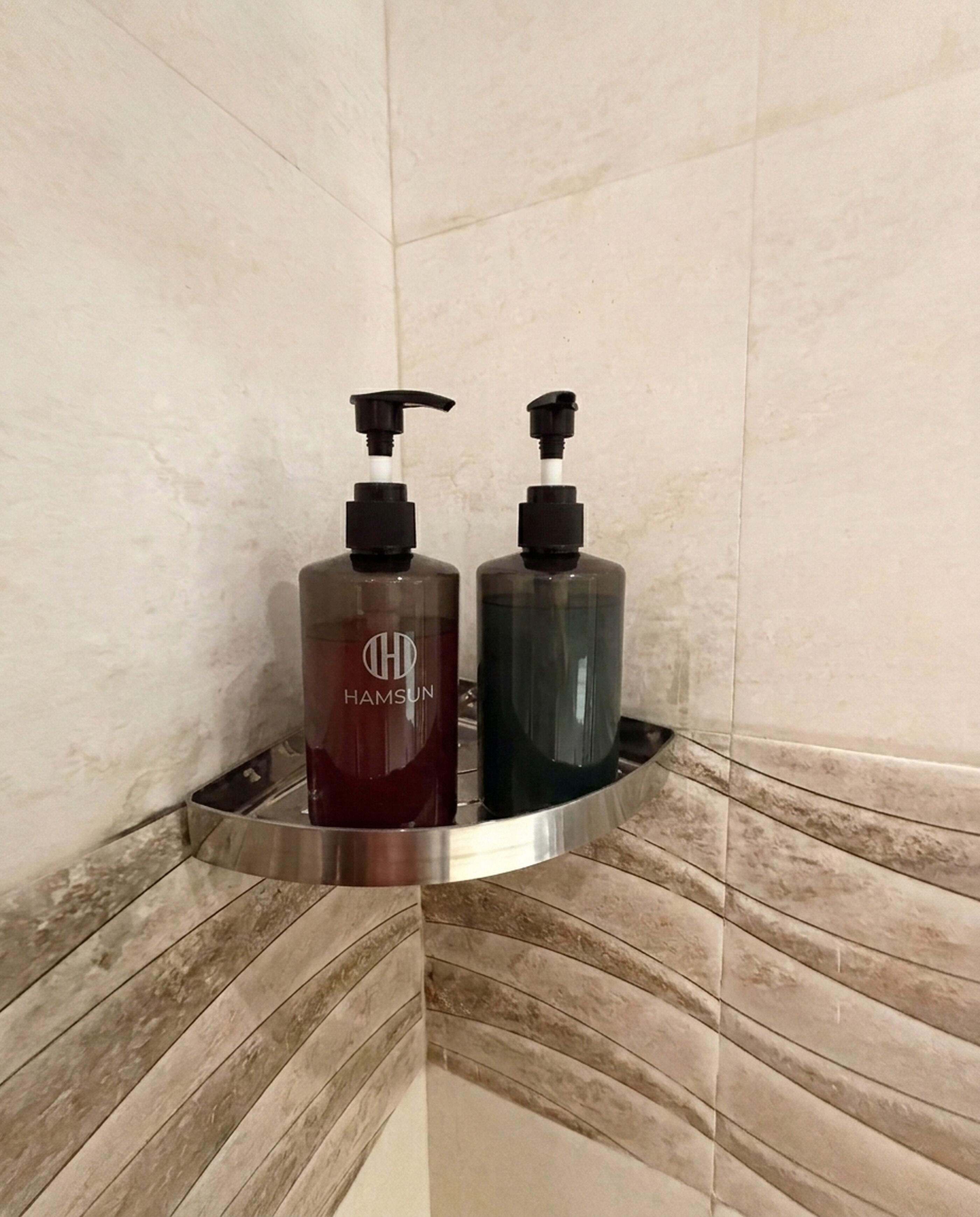 Two bottles of liquid soap on a metallic soap dish in a bathroom with tiled walls.