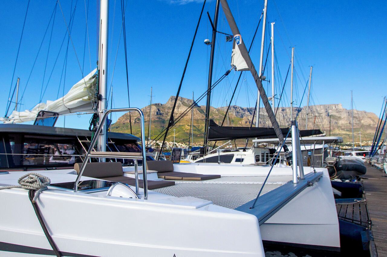 Un puerto deportivo con barcos amarrados, cielo despejado y montañas al fondo.