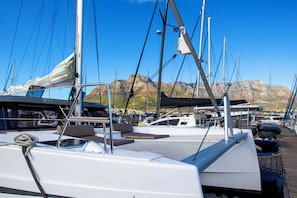 A marina with boats docked, a clear sky, and mountains in the background.