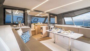 A modern yacht interior with a dining area, seating, and a view of the sea.