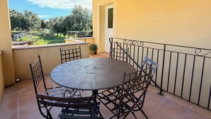 En overdækket terrasse med et rundt metalbord og stole, flisegulv og udsigt til grønt.