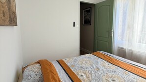 Et soveværelse med en seng, en loftsvifte, en grøn dør og et vindue med gardiner.