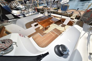A boat deck with a wooden table, a steering wheel, and a white railing.
