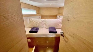 A compact room with a bed, two pillows, a wooden door, and a small drawer. - Sibenik Sun-soaked Sailing: A Luxurious Croatian Voyage (Pirovac)