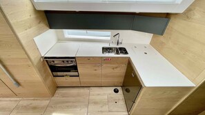 Eine kleine Küchenzeile mit Kochfeld, Backofen, Spüle und Holzschränken.