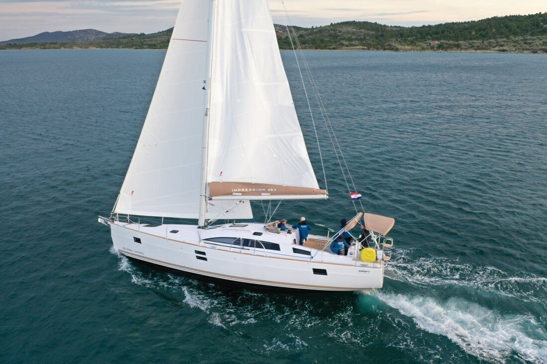 Un voilier à la coque blanche et à la grande voile blanche, naviguant sur des eaux calmes.
