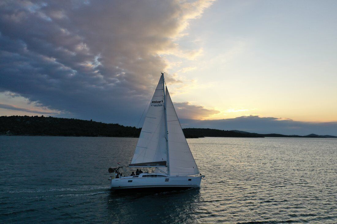 Een zeilboot op rustig water, ondergaande zon op de achtergrond.