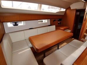 Un espacio interior compacto con una mesa de madera, asientos acolchados, una pequeña kitchenette y un tragaluz.