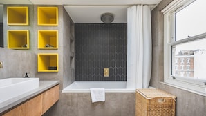 A modern bathroom with a bathtub, a window, and yellow storage shelves. - Modern Designer Townhouse, Earl's Court (London)
