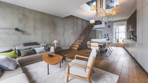 A modern living room with a sofa, coffee table, and chairs, a staircase leading to a kitchen, and a dining area. - Modern Designer Townhouse, Earl's Court (London)