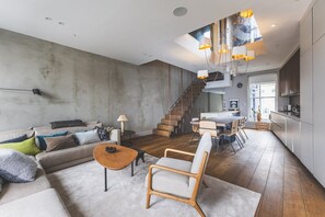 Ein modernes Wohnzimmer mit Sofa, Couchtisch und Sesseln, einer Treppe zum Küchenbereich und einem Essbereich.