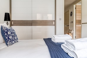 A hotel room with a bed, a nightstand with a lamp, a wardrobe, and a bathroom visible through an open door. - Modern Surrey Quays Flat (London)