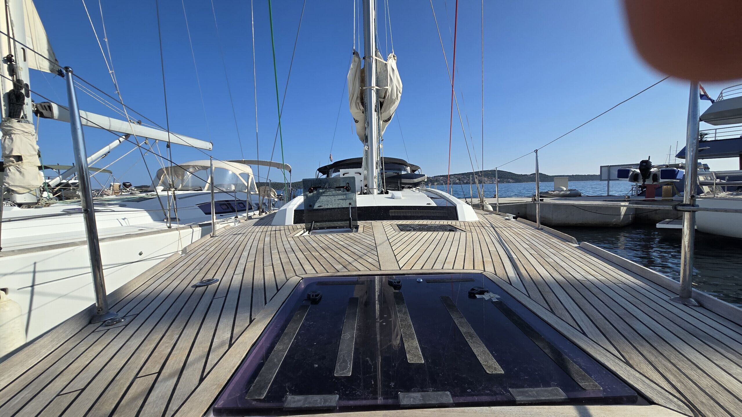 A wooden deck with a central seating area, a mast, and multiple boats docked in the background.
