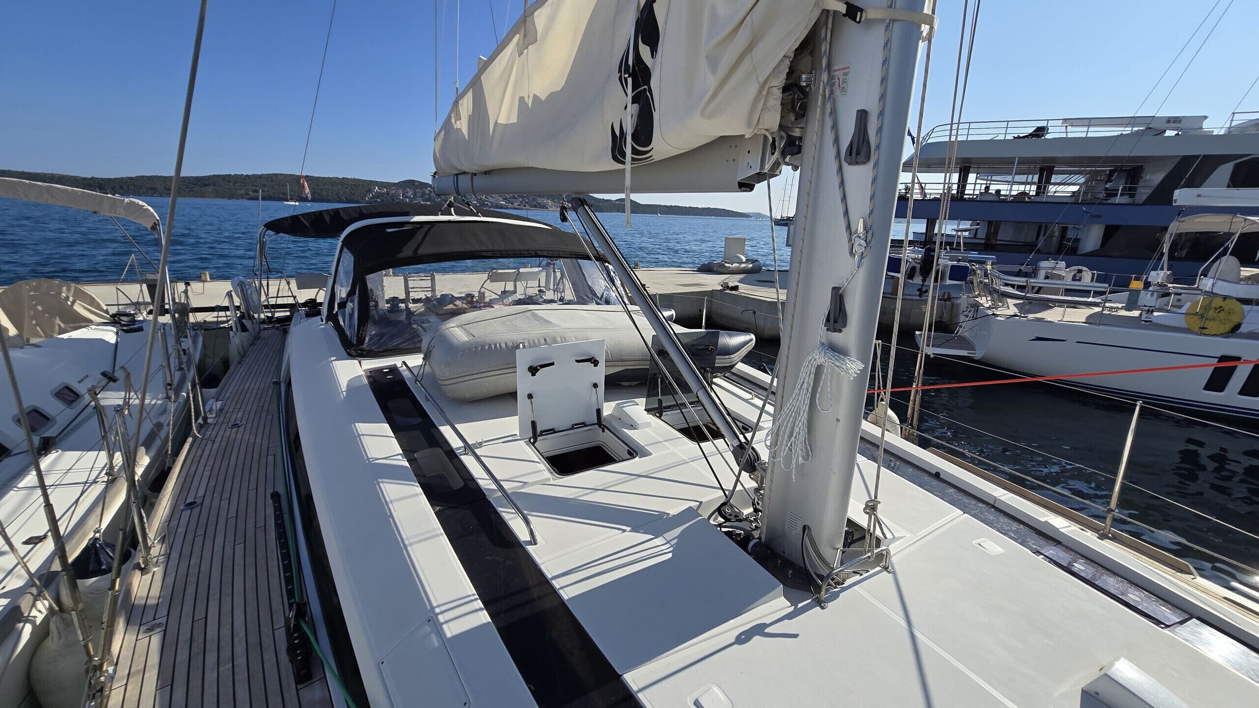 Ett däck på en segelbåt med ett avskärmat sittområde, en mast och utsikt över vattnet och andra båtar.