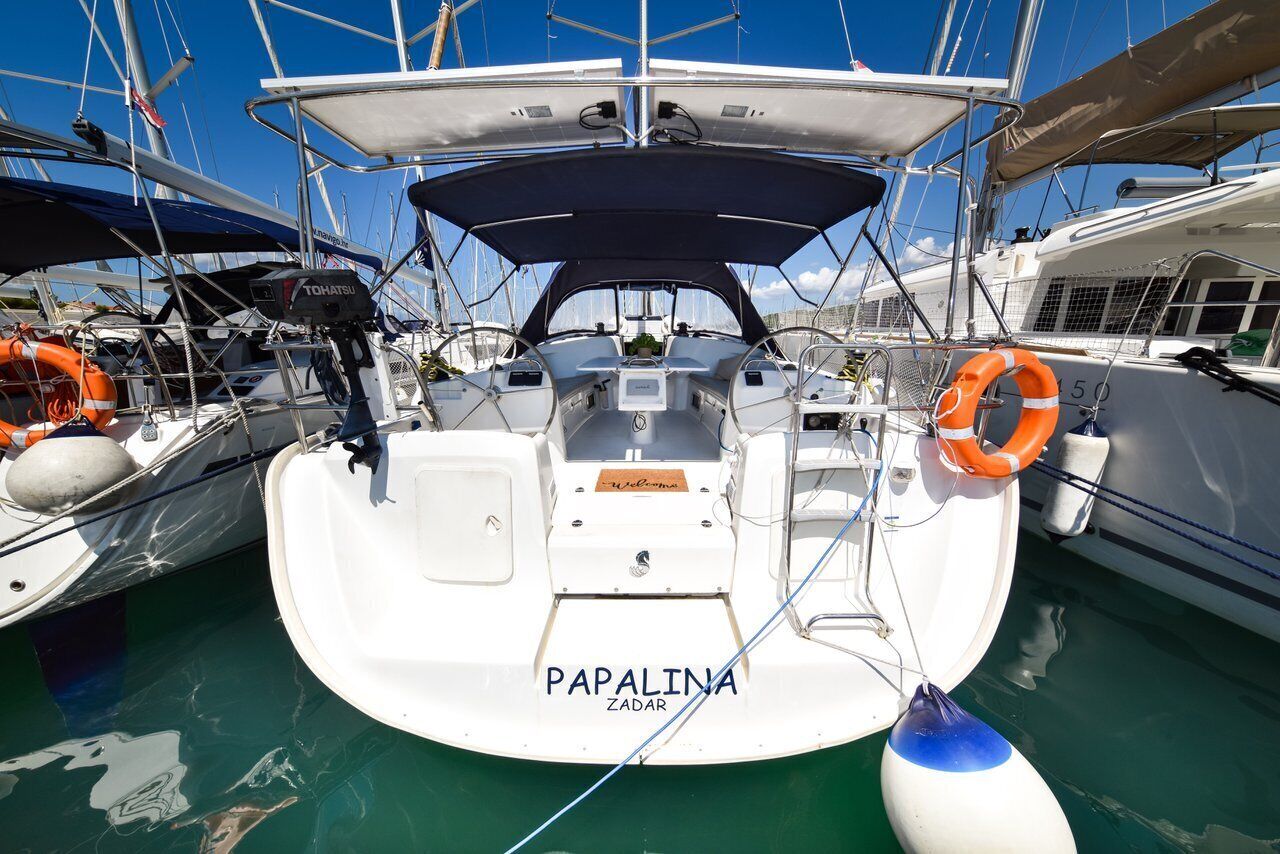 Een boot genaamd 'Papalina' afgemeerd in een jachthaven, met een overdekt dek, reddingsboeien en een stuurwiel.