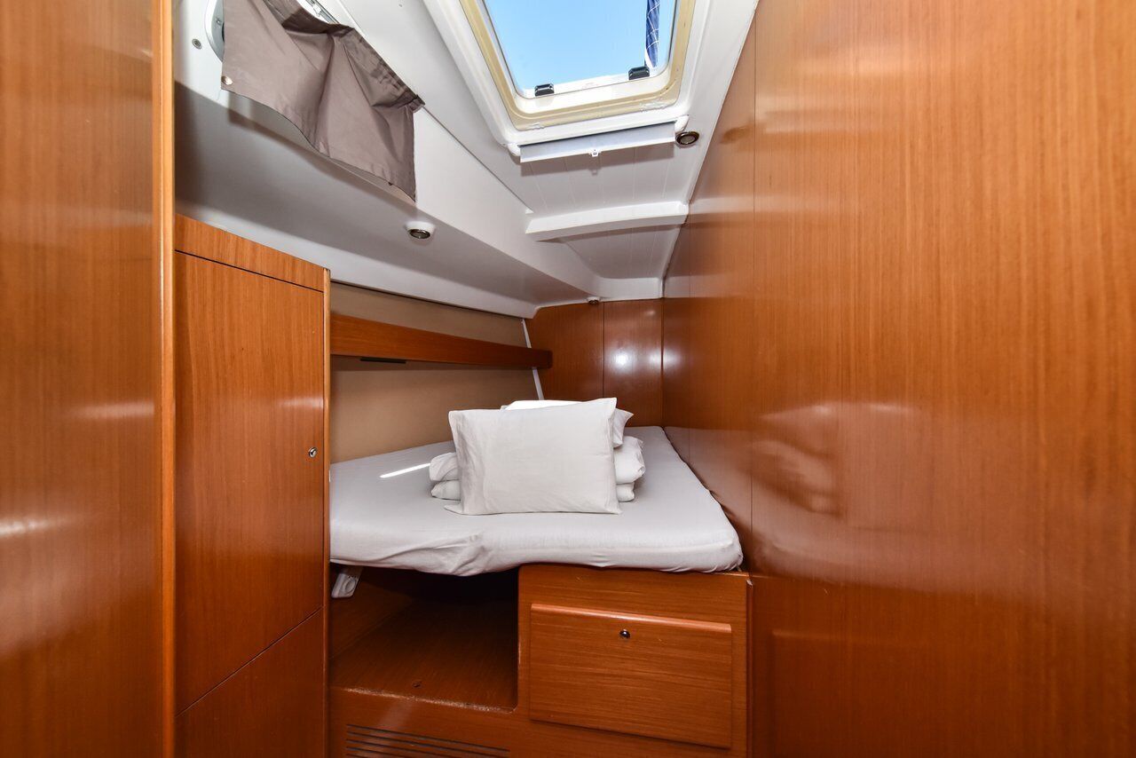 Una cabina compatta con un lucernario, un letto con lenzuola bianche e pannelli in legno.