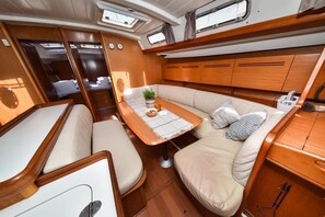 A compact, well-lit interior with a central seating area, a small table with a plant and a bowl, and wooden cabinetry. - Sun-Kissed Sailing Adventure in Zadar, Croatia (Bibinje)