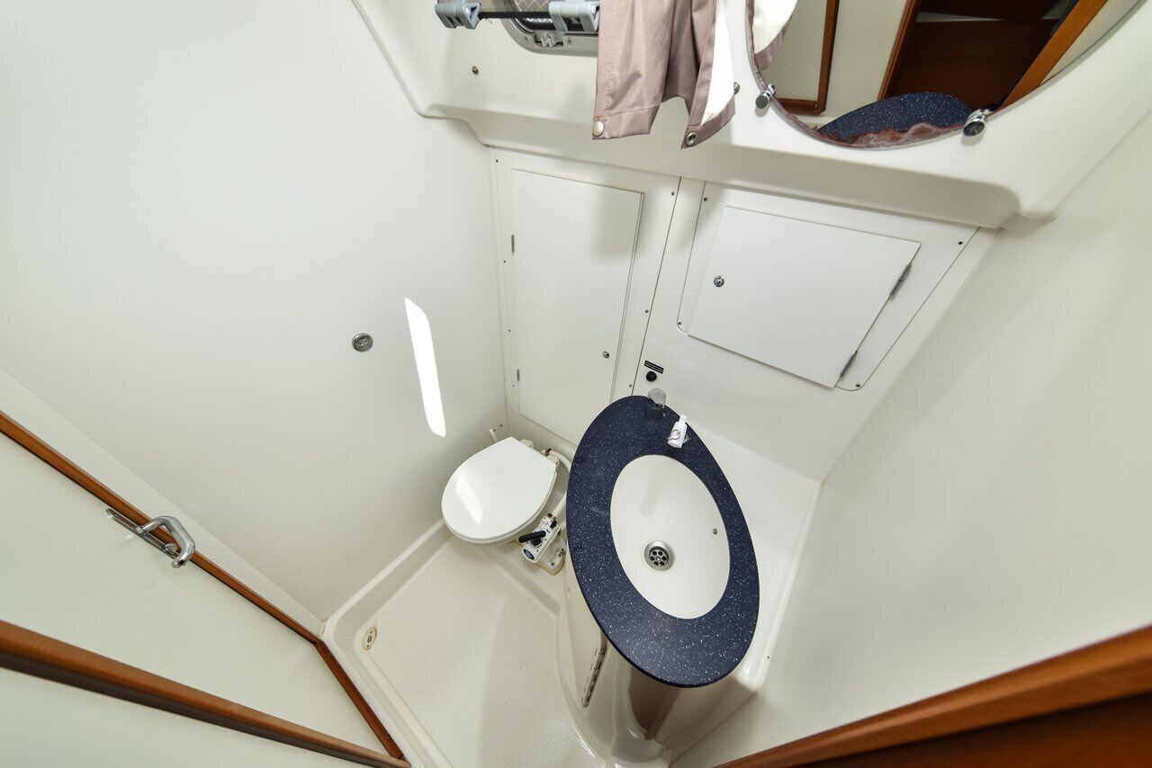 Un bagno compatto con un water bianco, un piccolo lavandino con piano d’appoggio scuro e uno specchio sopra il lavandino.