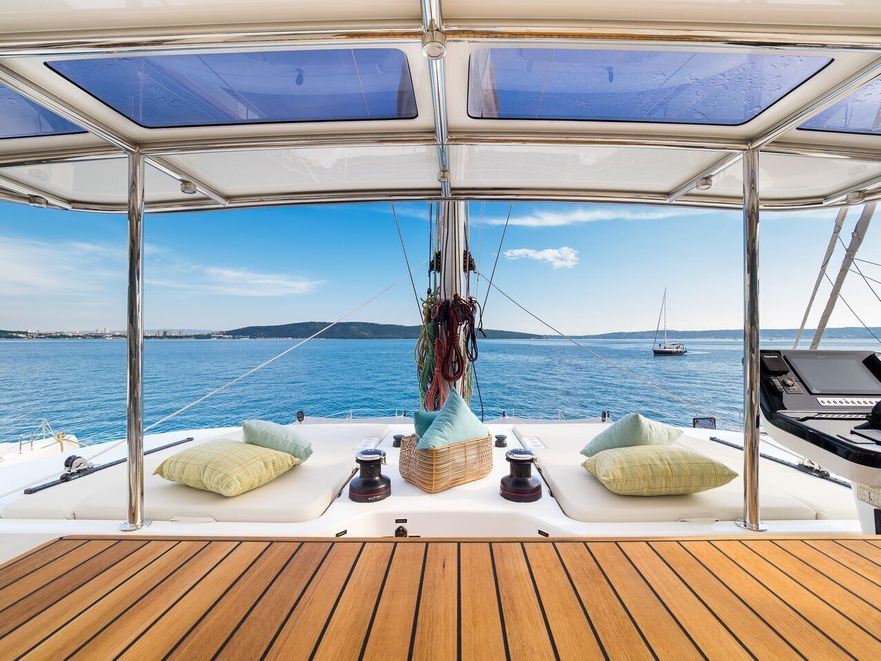 Un pont de bateau offrant une vue sur la mer, un plancher en bois et un espace détente avec des coussins et un panier.