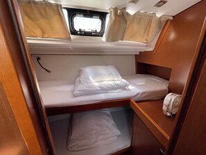 Een compact, goed verlicht interieur met een stapelbed, een klein raam met gordijnen en een houten hoofdbord.