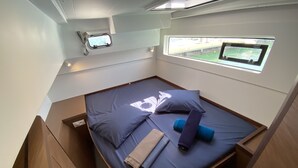 Een klein bed met kussens en dekbed, een raam met uitzicht en een plafondlamp.