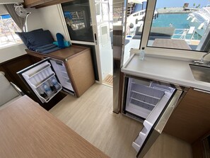 A compact kitchen with a refrigerator, a sink, and a window overlooking a marina. - Sun-Kissed Sailing Adventure in the Majestic Islas Baleares (Ibiza / Eivissa)