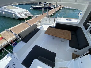 A yacht deck with a seating area, a table, and a view of other boats at the marina. - Sun-Kissed Sailing Adventure in the Majestic Islas Baleares (Ibiza / Eivissa)