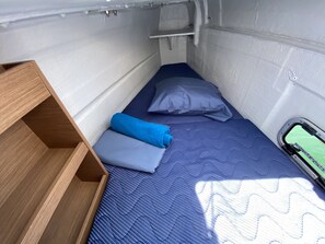 A small, narrow room with a single bed, a wooden shelf, and a small table.