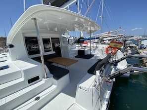 A yacht with a covered seating area, a small table, and a view of the marina.