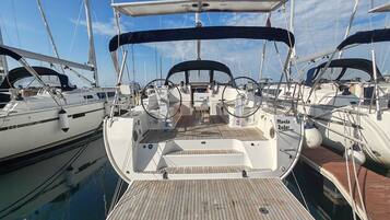 A marina with multiple sailboats docked, featuring a wooden deck, steering wheel, and a covered area.