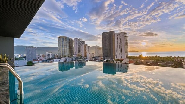 Una piscina infinita en la azotea con vista a la ciudad, incluyendo rascacielos y montañas al fondo.
