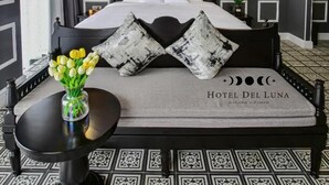 Habitación de hotel con una cama, una mesita de noche con un jarrón de flores y una lámpara de pared.