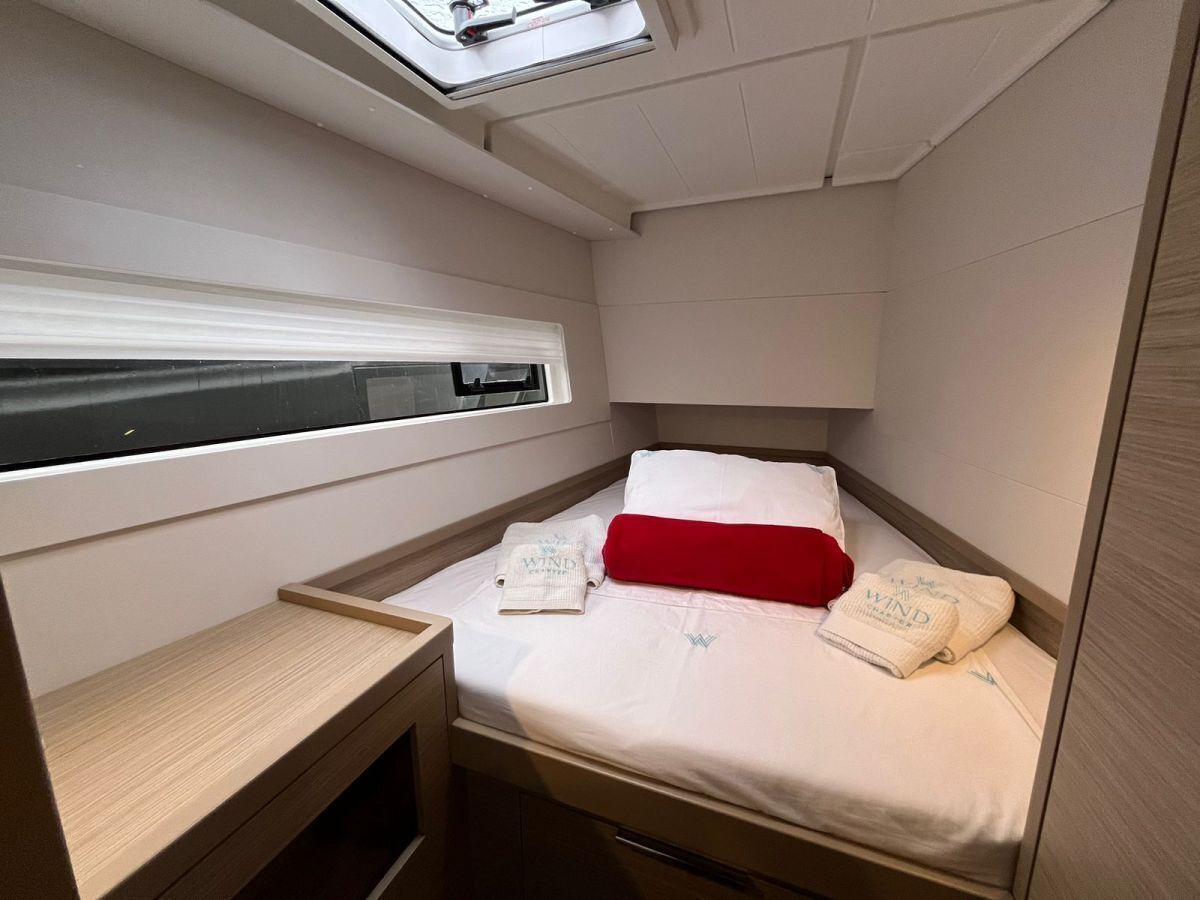 Una habitación pequeña con cama, una mesita de noche, una ventana y un tragaluz.