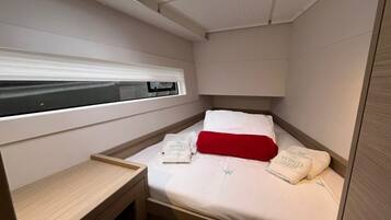 Una habitación pequeña con cama, una mesita de noche, una ventana y un tragaluz.