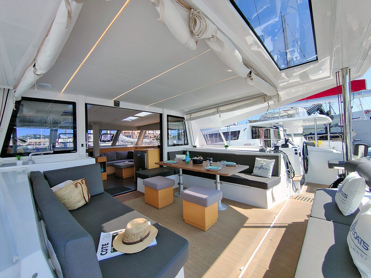 A yacht interior with a sofa, ottomans, a dining table, and a steering wheel area.