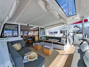 A yacht interior with a sofa, ottomans, a dining table, and a steering wheel area.
